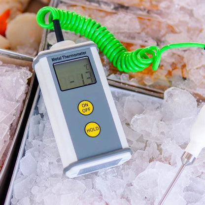 Un Thermomètre étanche de Thermomètre.fr avec un cordon enroulé vert indique une lecture de -1,7°C. Cet appareil CaterTemp en métal, placé sur un lit de glace aux côtés d'autres objets, présente un boîtier en aluminium robuste assurant durabilité et fiabilité.