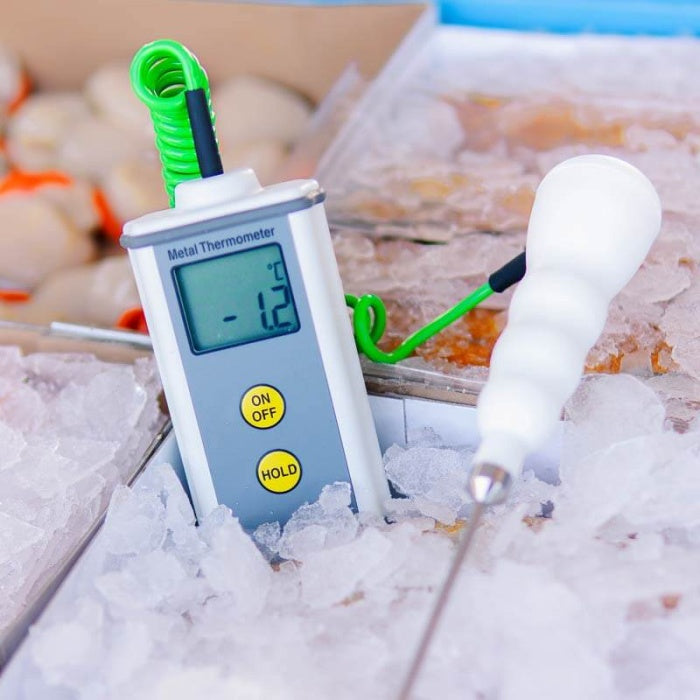 Un thermomètre Thermomètre.fr CaterTemp en métal, doté d'un boîtier robuste en aluminium, affiche une température de -1,2°C lorsqu'il est inséré dans un récipient de glace avec des fruits de mer en fond.