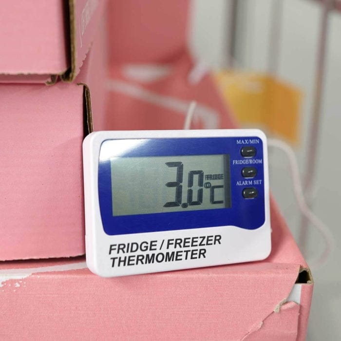 Un Thermomètre alarme pour réfrigérateur / congélateur de Thermomètre.fr, affichant une température de 3,0°C, est placé sur des cartons roses, assurant une surveillance précise grâce à sa fonction d'alarme sonore.