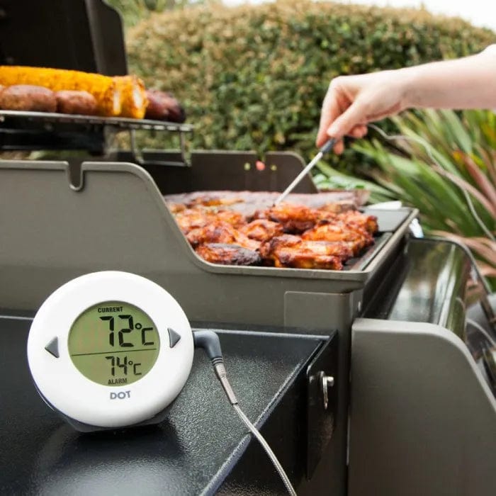 Gros plan d'une personne vérifiant la température d'une viande sur un barbecue à l'aide d'un Thermomètre DOT pour quatre de Thermomètre.fr, doté d'un affichage numérique indiquant 72°C et d'une alarme sonore réglée sur 74°C, garantissant une cuisson facile.