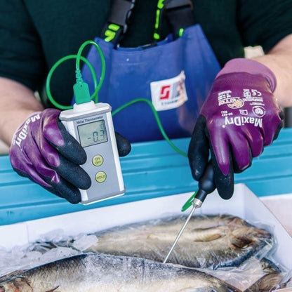Une personne portant des gants tient un Thermomètre.fr Therma K en métal inséré dans un poisson, avec une lecture de -0,3 sur l'écran. Les poissons sont entourés de glace dans un récipient bleu.